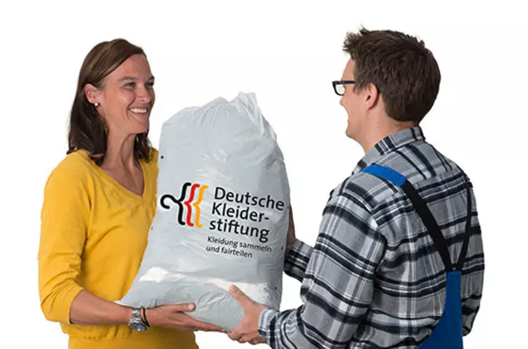 Ein Mann übergibt einer Frau einen Kleidersack mit dem Logo der Deutschen Kleiderstiftung
